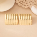 Détail de boucles d'oreilles carrées dorées à texture ondulée sur fond beige épuré - Doré