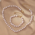 Detail of elegant white pearl necklace and bracelet set with gold clasps on satin fabric - White