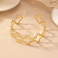 Detailed view of a gold open cuff bracelet with hollow clover patterns on a warm stone surface - Gold