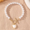 Détail d'un bracelet de perles avec pendentif cœur et fermoir OT doré sur tissu - Blanc