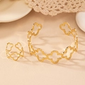 Detailansicht eines goldenen Armreifs und Ring-Sets mit Blumen-Ausschnitten auf Stoff - Armband- und Ring-Set / Gold