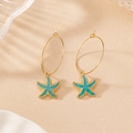 Detail of golden starfish earrings with blue enamel finish and elegant texture - Teal