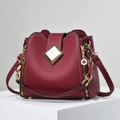 Sac seau bordeaux en cuir grainé avec boucle dorée élégante posé sur un socle blanc - Bordeaux
