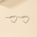 Detailed close-up of hollow silver heart stud earrings on a clean beige surface - Heart Studs