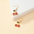 Fashionable red cherry drop earrings with gold hooks and black leaves on a beige display - Gold