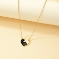 Golden heart necklace with black enamel handshake pendant on minimalist display - Gold