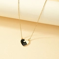Golden heart necklace with black enamel handshake pendant on textured display - Gold