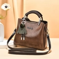 Dark brown oil wax PU leather handbag with silver logo and green doll pendant detail - Brown