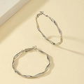 Boucles d'oreilles créoles torsadées argentées au design ondulé sur fond beige - Or blanc