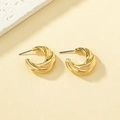 Detailed view of gold twisted C-shape hoop earrings with spiral texture on stone background - Gold