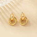 Boucles d'oreilles créoles dorées géométriques sur un fond minimaliste beige élégant - Doré