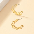 Détail de créoles dorées en forme de C avec motif ajouré LOVE sur fond de texture beige - Doré