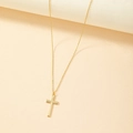 Collana con croce dorata minimalista e pendente testurizzato su sfondo color albicocca - Oro