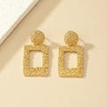 Pendientes colgantes geométricos rectangulares dorados con textura martillada en fondo beige - Dorado