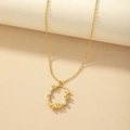 Elegante collar dorado con perlas y colgante de flor sobre un fondo de tono cálido - Dorado