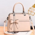 Pale pink leather handbag with large bow detail and heart-shaped metal hardware on wooden desk - Khaki