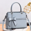 Detail of light blue bow handbag with heart charm on a minimalist wooden table - Blue