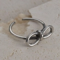 Close-up of a silver bow-shaped vintage steel ring on a textured beige stone background - Polished Bow Knot Style (R558)
