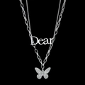 Primer plano de collar de doble capa plateado con colgante de mariposa y letras Dear - Estilo de Doble Capa con Letra y Mariposa / Color Acero