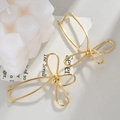 Vista detallada de pendientes dorados con forma de lazo en un elegante soporte minimalista - Pendientes de lazo hueco irregular