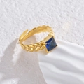 Macro-opname van goudkleurige gevlochten ring met blauwe steen en open ontwerp - Donkerblauwe Vierkante Zirkoon Ring
