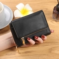 Compact black litchi leather wallet with golden zipper shown on a wooden desk - Black
