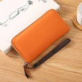 Long orange ostrich pattern PU leather clutch wallet with wrist strap on a wooden desk - Orange