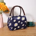 Isolierte dunkelblaue Lunchtasche mit Gänseblümchenmuster und braunen Webgriffen auf Holz - Blaues Gänseblümchen