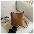 Detail of a brown suede bucket bag featuring a minimalist matte finish on a sofa - Tan