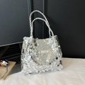 Silberne Pailletten-Tragetasche mit geflochtenen Ledergriffen und Metalllogo auf Tisch - Silber