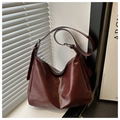 Detalle de bolso hobo granate en cuero suave con hebillas plateadas junto a una ventana - Rojo