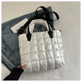 Detail of white quilted puffer tote bag with black contrast strap on denim backdrop - White