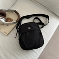 Bolso bandolera minimalista de nailon negro para mujer con logo en sofá beige - Negro