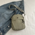 Kleine legergroene nylon crossbodytas met verstelbare riem op denim achtergrond - Groen