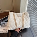 White quilted tote bag with gold chain strap and logo on a dark leather surface - White