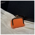 Detailed view of mini orange leather kiss-lock jewelry pouch on white silk fabric - Orange