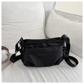 Vista detallada del bolso bandolera de nailon negro con correa ajustable en cama blanca - Negro