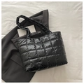 Detail of black quilted puffer tote bag on neutral fabric with minimalist fashion props - Black