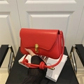 Red leather baguette bag featuring golden C-clasp and woven knot shoulder strap details - Red