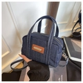 Detail van donkerblauwe denim handtas met witte stiksels en bruin lederen accenten - Blauw