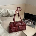Dark red shiny leather Boston bag with pocket details in a modern lifestyle setting - Red