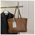 Dettaglio di una borsa tote in ecopelle marrone con targhetta grigia su gruccia - Marrone