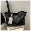 Detalle del bolso tote negro grande con textura y colgante en un taburete blanco - Negro