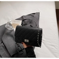 Detail of black quilted crossbody bag with silver clasp and chain on grey suit - Black
