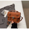 Detailed view of brown vintage crossbody bag with metal lock and decorative straps on soft bedding - Brown