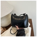 Detail of black glossy faux leather dumpling bag with slim strap on a wooden desk - Black