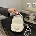 Close-up of cream mini backpack featuring lace trim, bow detail and silver chain strap - White