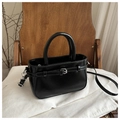 Detalle de bolso en cuero negro brillante con hebilla decorativa y costuras finas - Negro