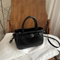 Chic black glossy leather handbag with buckle strap on a minimalist wooden chair - Black