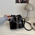 Glossy black bucket bag with silver chain drawstring and pearl detail on white desk - Black
